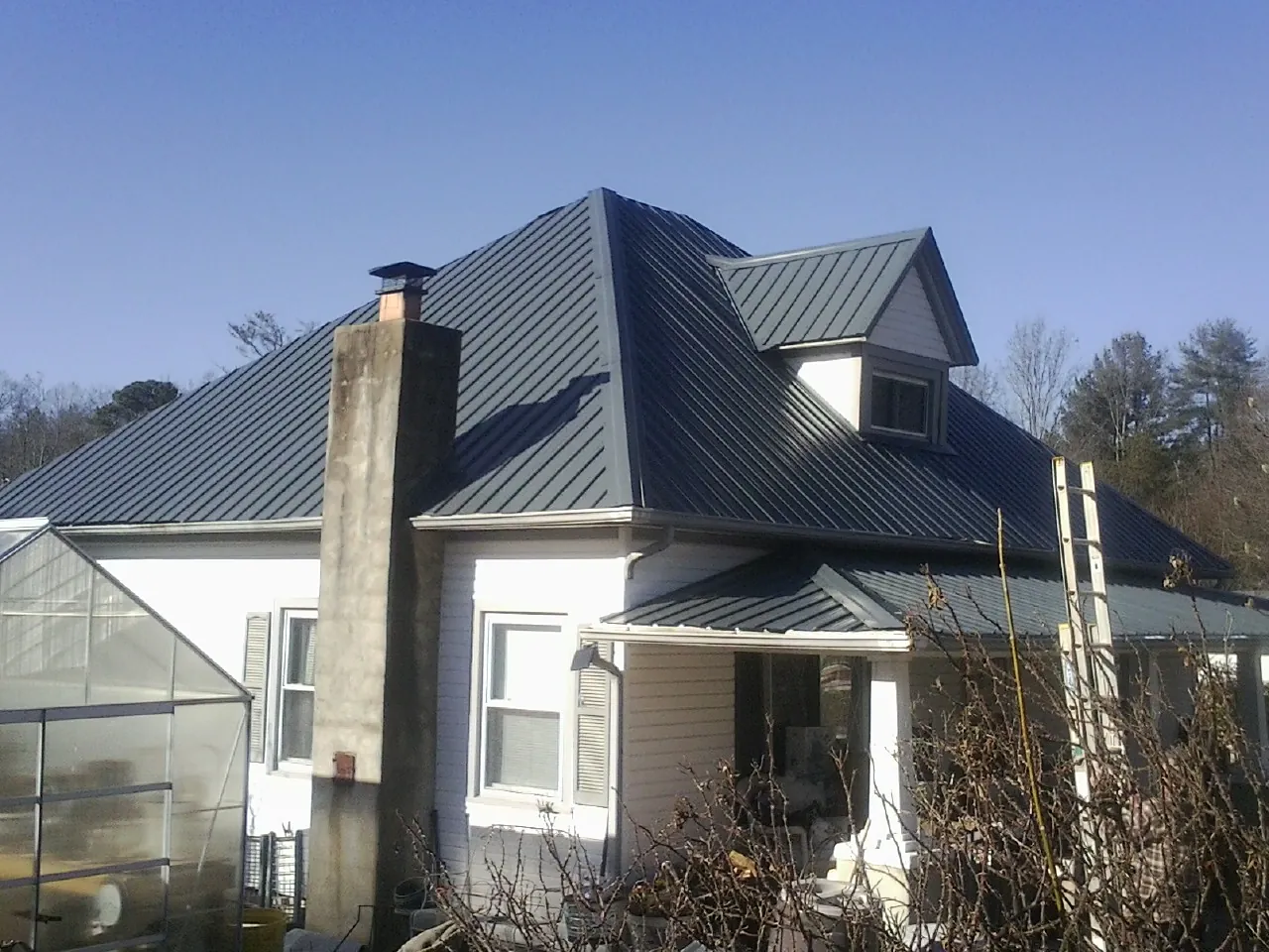 Dark blue standing seam metal roof on a white farmhouse with dormer — Slate & Tile Roof Repair by Roofing Brothers in Madison