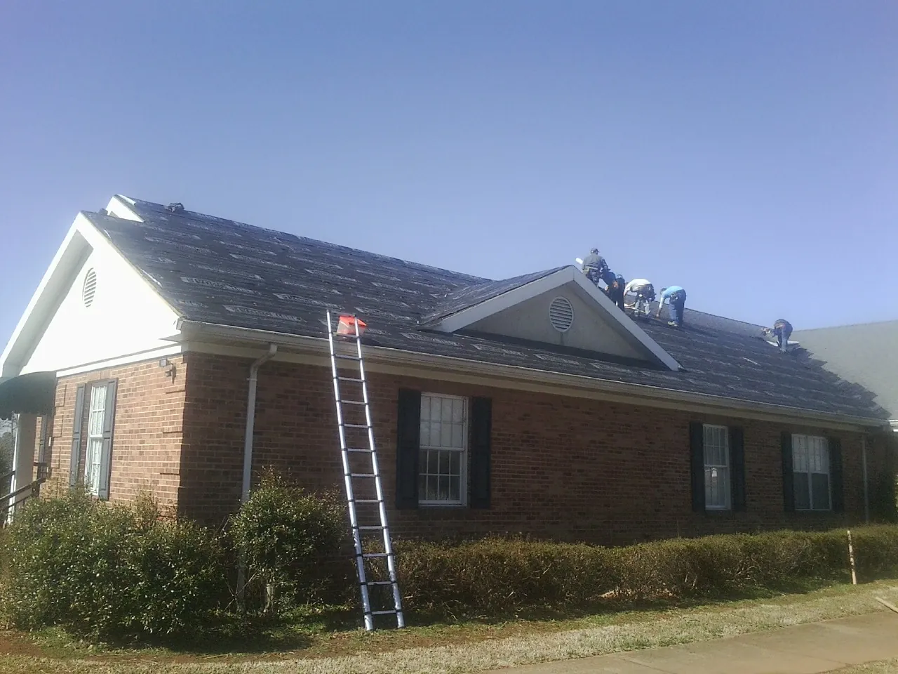 Crew tearing shingles off a brick ranch roof with a ladder set — Emergency Roof Repair work by our crew in Madison